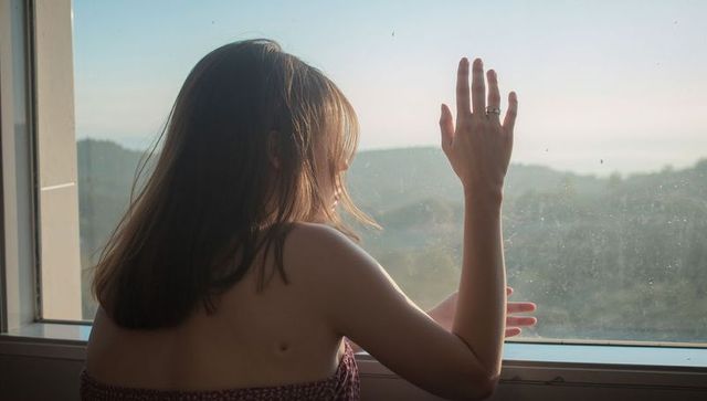 Woman pressing ringed hand against window, gazing at coastal hills and water