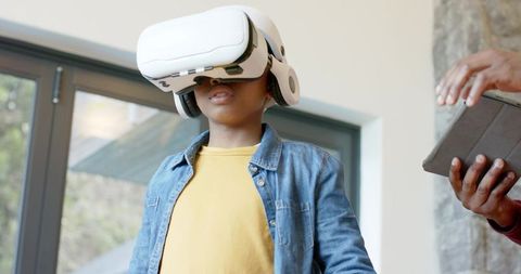 Young African American boy experiencing VR headset with caregiver supervising home learning