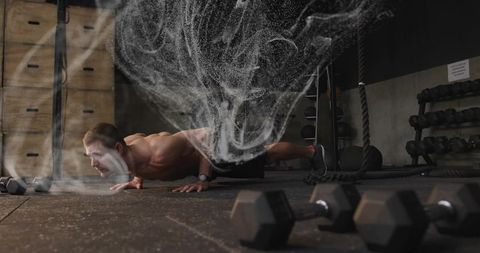 Shirtless athlete performing low push-up with dramatic chalk cloud in industrial gym