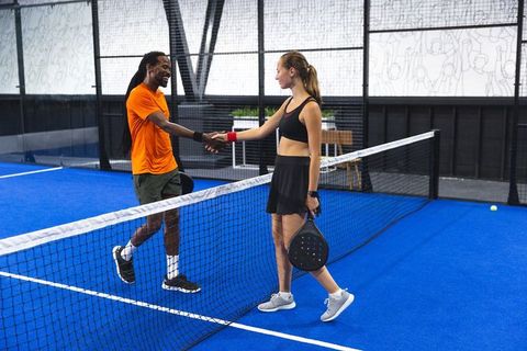 Diverse players shaking hands on padel court after match