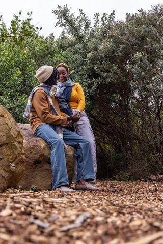 Cozy autumn moment: african american couple holding hands on boulder by forest trail