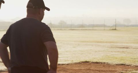 Backlit coaches watching sunlit baseball diamond at golden hour coaching team practice