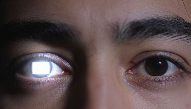 Macro close-up of male eyes reflecting rectangular screen light, low-light tech portrait