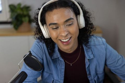 Non-binary podcaster recording with microphone and headphones in cozy home studio