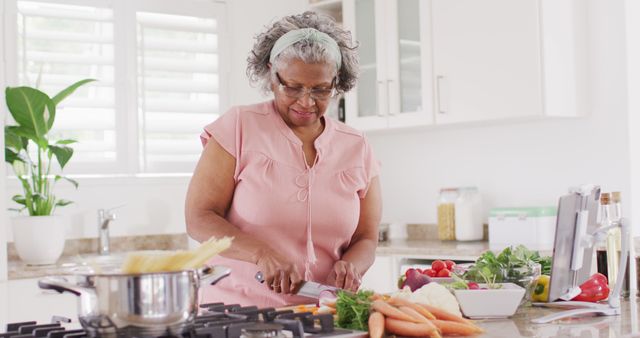 Senior woman chopping carrots and preparing vegetables in a modern kitchen. Perfect for topics including healthy eating, senior lifestyle, home cooking, nutrition, and culinary arts. Highlights simplicity and positive lifestyle choices for older adults.
