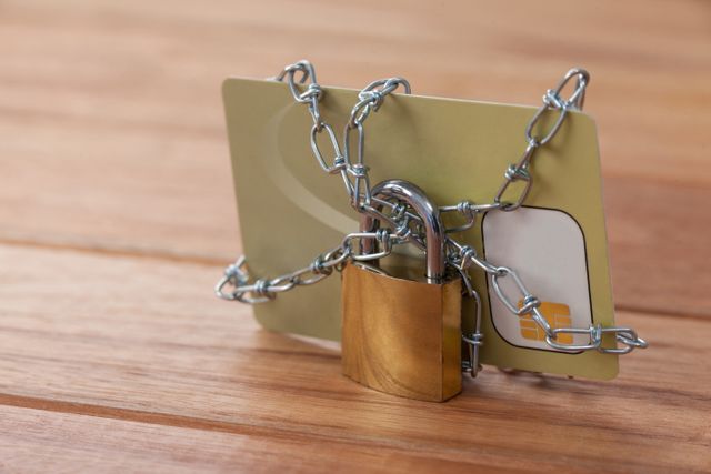 Smart card wrapped in chain and secured with padlock on wooden surface. Represents concepts of data protection, financial security, and cyber security. Ideal for illustrating articles on secure transactions, privacy measures, and encryption technologies.