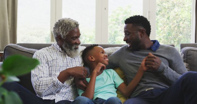 African American grandfather, father, and son smiling and enjoying time together on couch. This scene captures familial love, bonding, and joyful interaction in a home interior. Great for themes involving family relationships, generational connections, parenting, and home life.