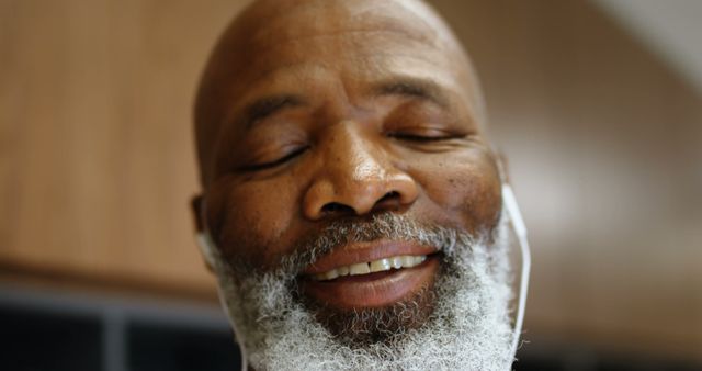 Elderly man with white beard smiling and closing his eyes, enjoying music through headphones. Close-up image captures contentment and tranquility. Great for promoting relaxation, mental well-being, senior lifestyle products, and multimedia content focused on positive emotions.