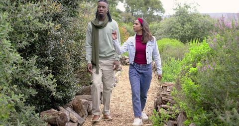 Diverse Couple Walking Woodchip Trail Through Lush Park Foliage Conversing Casually