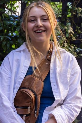 Young woman smiling in garden wearing white shirt and brown leather crossbody bag