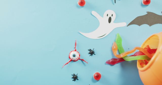 Colorful and fun Halloween-themed items including a white ghost cutout, toy eyeballs, small black spider shapes, and bright gummy worms. This image could be used for Halloween party invitations, greeting cards, social media posts, blog articles, and any other projects seeking a playful and festive Halloween aesthetic.