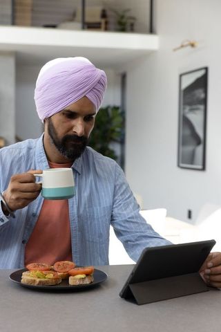Mid adult man using tablet with coffee and sandwiches in minimalist kitchen