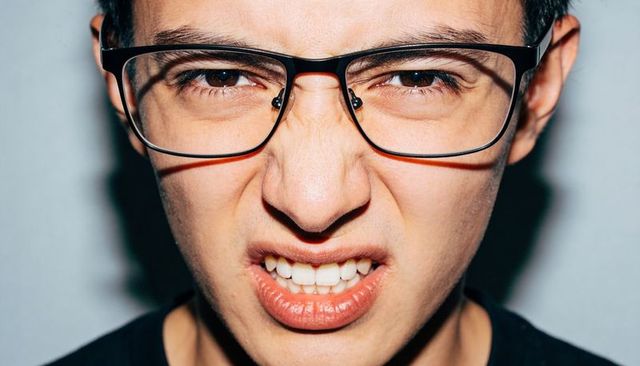 Asian male grimacing and squinting wearing glasses closeup high-contrast studio portrait