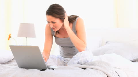 Woman Relaxing on Bed Using Laptop in Bright Interior