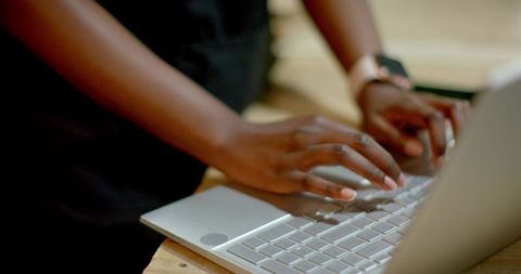 Typing hands on silver laptop with smartwatch on wrist, warm wood desk closeup