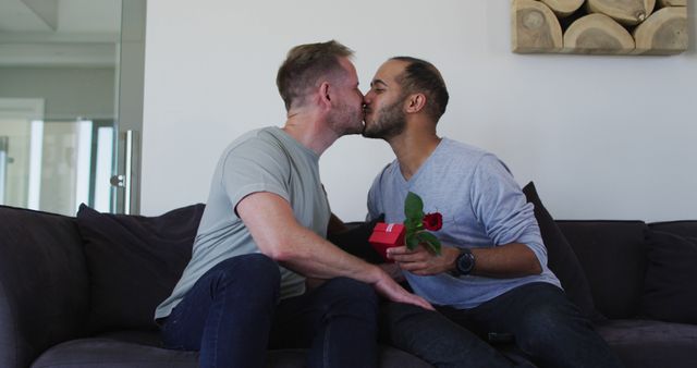 Multi ethnic gay male couple embracing one holding a gift. enjoying staying at home in self isolation in quarantine lockdown.