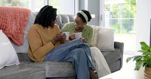 African American Couple Sharing Coffee and Laughter on Cozy Sofa in Bright Living Room