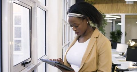 African american woman using tablet by grid windows in modern minimalist office, focused