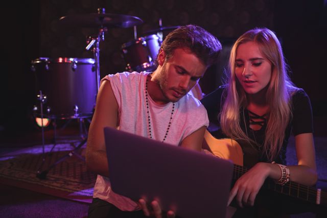 Young male and female musicians using laptop while practicing in nightclub