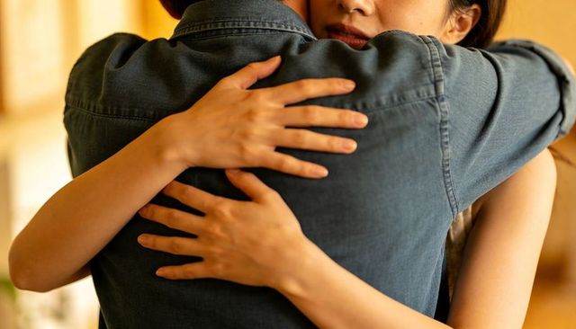 Couple embracing tightly in warm softly lit room, expressing intimacy, comfort and connection
