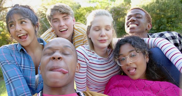 This image shows a diverse group of young friends making silly faces while enjoying time outdoors. Perfect for visual content related to friendship, youth activities, outdoor fun, diversity, and multiculturalism.