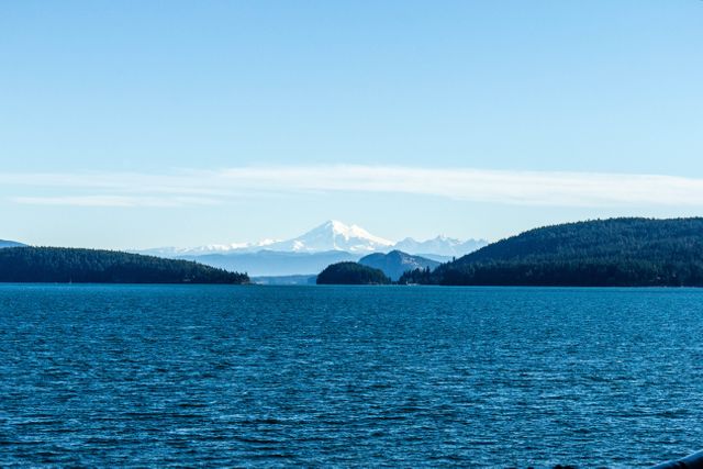 Showing calm water with forested islands, a snow-capped mountain in background adds scenic beauty. Perfect for use in travel promotions, nature-inspired content, or themes about tranquility and natural beauty.