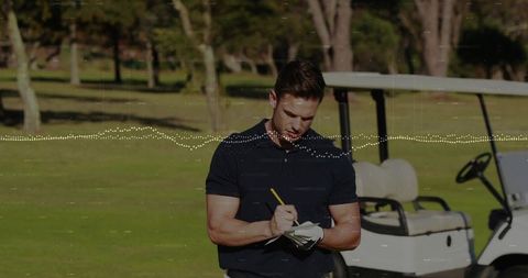 Man writing golf scorecard on sunlit fairway by cart, recording scores and notes