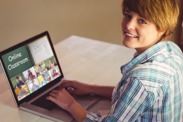 Student attending an online classroom session on a laptop and smiling. Ideal for use in content about remote education, virtual learning environments, e-learning platforms, digital classrooms, and educational technology solutions.