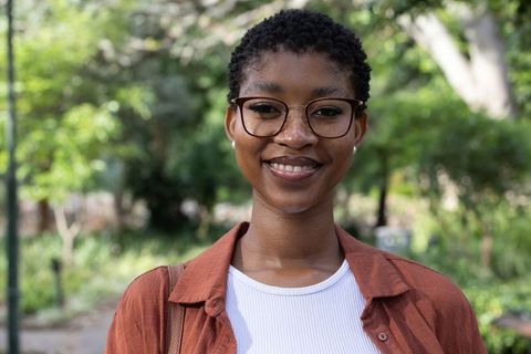 African woman smiling outdoors wearing tortoiseshell glasses and rust jacket portrait