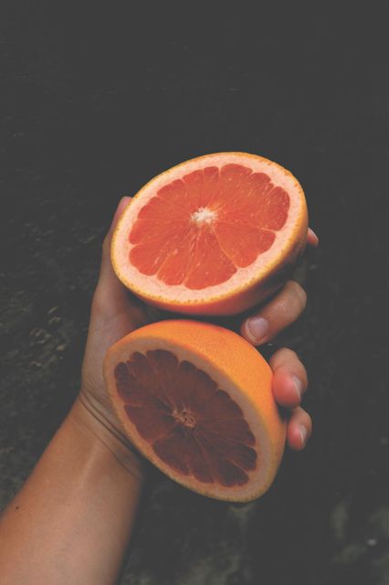 Image of a person holding two halves of a sliced grapefruit against a dark background. Perfect for promoting healthy eating, nutrition blogs, organic fruit markets, wellness articles, and vitamin C-rich foods.