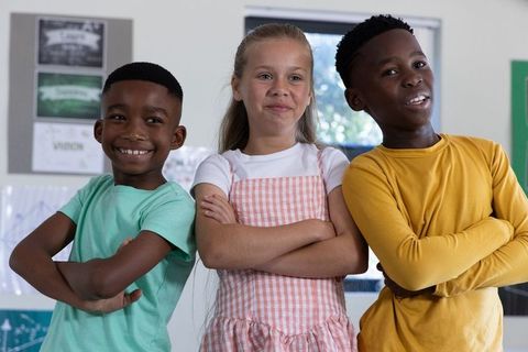 Confident diverse school children standing and smiling with arms crossed in bright classroom