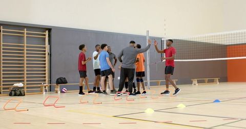 Diverse male volleyball team practicing agility and teamwork drills in indoor school gym