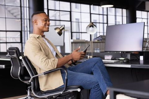 Smiling African American professional holding smartphone and scrolling in modern office