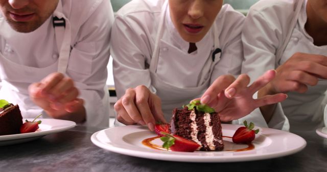 Chefs engaged in intricate chocolate cake decoration, seen from a low angle in a commercial kitchen. Useful for themes on culinary arts, professional cooking, food presentation, team collaboration, and gourmet desserts.