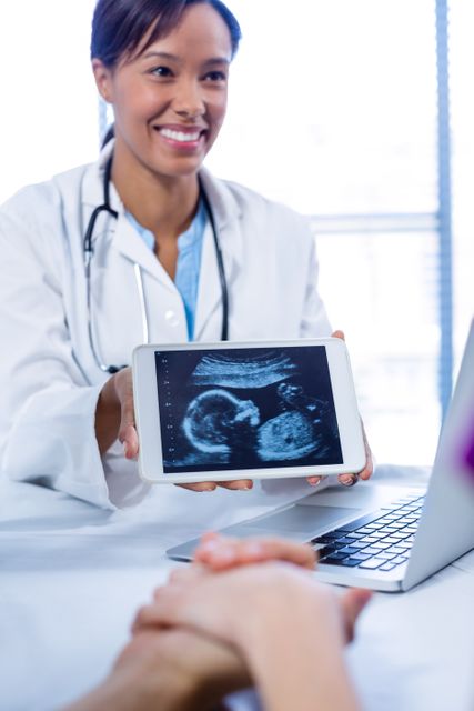 Doctor presenting ultrasound scan on digital tablet during patient consultation in hospital. Ideal for use in healthcare, prenatal care, and medical technology content.