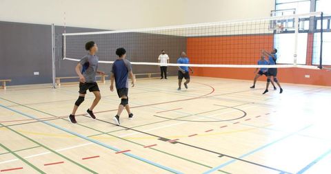 Diverse male volleyball team playing indoors jumping to block and spike on gym court
