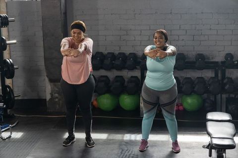 African american women stretching and smiling during workout in gym with dumbbells