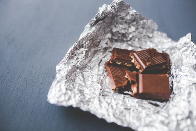 Unwrapped pieces of chocolate bar on crumpled foil, perfect for websites, blogs, or articles related to food, desserts, and recipes. Ideal for illustrating indulgence, snacks, or sweet treats.