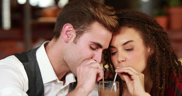 A young Caucasian man and a young woman with curly hair are sharing a drink through two straws, with copy space. Their close proximity and shared activity suggest a romantic or intimate connection.