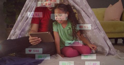 Father and daughter sharing tablet inside cozy teepee, smiling amid floating social icons