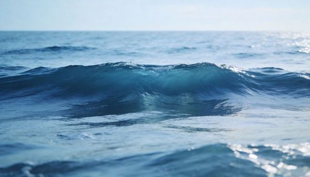Turquoise ocean wave cresting at open sea with translucent crest and sunlit ripples