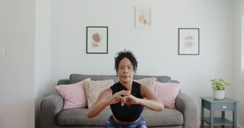 African american woman performing squat workout in living room for home fitness strength