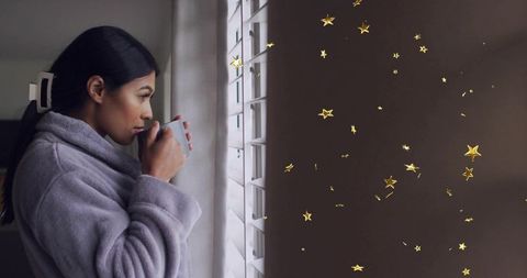 Woman in robe sipping coffee by shuttered window with floating gold stars, morning calm