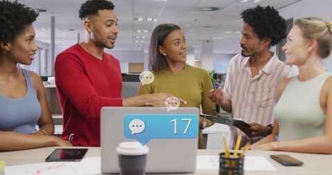 Multiracial team collaborating around laptop with chat notification 17 in modern office