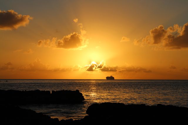 Stunning view of the sun setting over the ocean with a cruise ship visible in silhouette. Perfect for travel, vacation, maritime themes, and nature-related projects. It captures the peaceful, calming essence of a maritime evening.