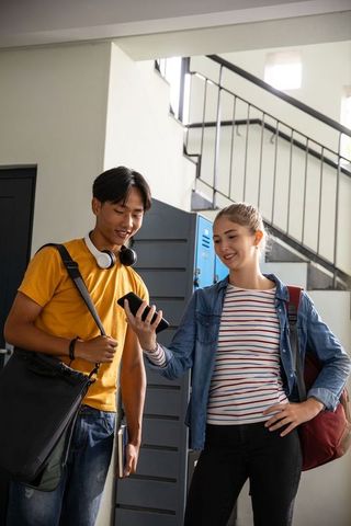 Teen Students Sharing Smartphone in School Hallway Near Lockers and Staircase