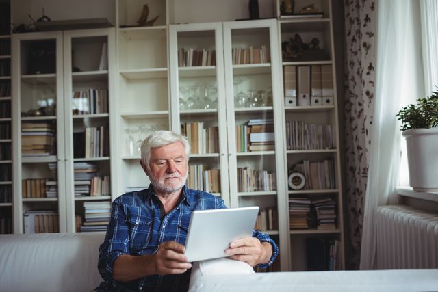 Senior man sitting on sofa and using digital tablet in living room