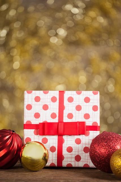 Festive close-up featuring a wrapped gift box with red polka dots and a red ribbon, accompanied by Christmas baubles on a wooden table. Perfect for holiday-themed promotions, advertisements, greeting cards, and festive blog posts.