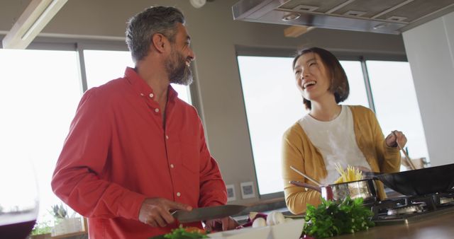 Couple enjoys cooking together while smiling and sharing a moment in a contemporary kitchen. Great for lifestyle blogs, culinary websites, and advertisements promoting home-cooked meals and family bonding.