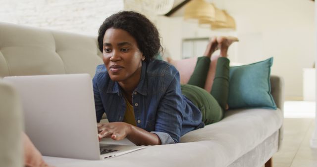 Image of happy african american woman on sofa using lapotp. leisure and relax, spending free time with technology at home.